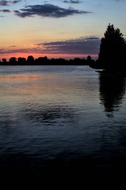 Sonbaharda ağaçlarla çevrili bir gölün üzerinde gün batımı