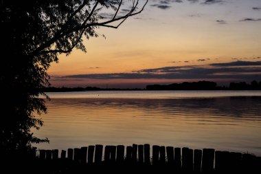 Sonbaharda ağaçlarla çevrili bir gölün üzerinde gün batımı
