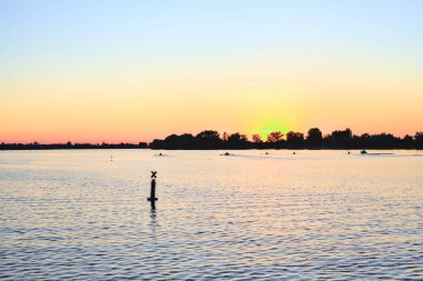 Bir gölün üzerinde gün batımı ve arka planda bir orman.