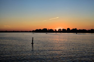 Bir gölün üzerinde gün batımı ve arka planda bir orman.