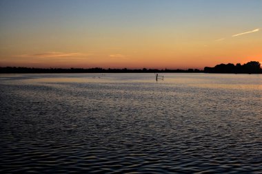 Bir gölün üzerinde gün batımı ve arka planda bir orman.