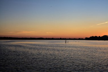 Bir gölün üzerinde gün batımı ve arka planda bir orman.