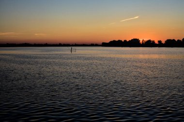 Bir gölün üzerinde gün batımı ve arka planda bir orman.