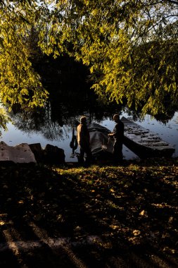 İnsanlar gün batımında nehir kenarında birkaç teknenin yanında konuşuyor.