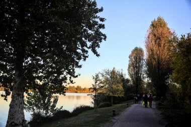 Sonbaharda gün batımında nehir kenarındaki bir parkta gezinen insanlarla dolu çakıl yolu.