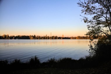 Alacakaranlıkta göl ve karşı kıyıda bir park.