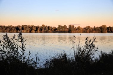 Alacakaranlıkta göl ve karşı kıyıda bir park.