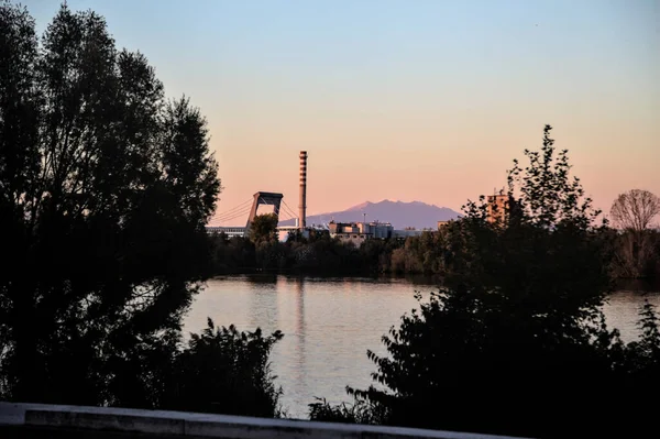 Alacakaranlıkta ağaçların çerçevelediği fabrika.