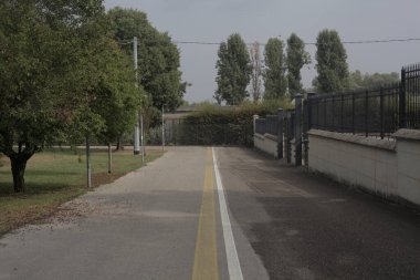 Bulutlu bir günde parkın yanında metal bir ızgarayla çevrili bisiklet yolu.