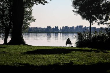 Gün batımında bir parkta gölün kıyısında oturan balıkçı.