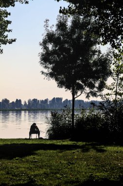 Gün batımında bir parkta gölün kıyısında oturan balıkçı.