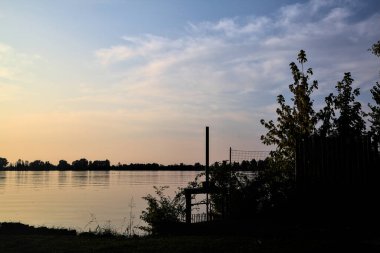 Gün batımında gölde ağaçların siluetiyle çerçevelenmiş.