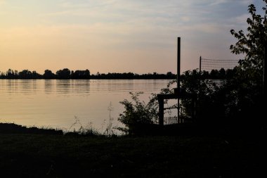 Gün batımında gölde ağaçların siluetiyle çerçevelenmiş.