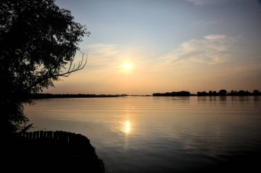 Gün batımında gölde ağaçların siluetiyle çerçevelenmiş.