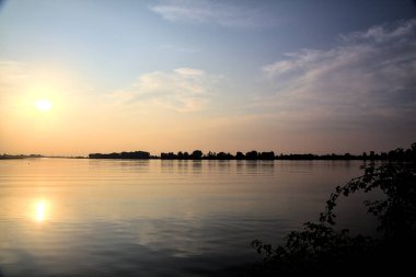Gün batımında gölde ağaçların siluetiyle çerçevelenmiş.