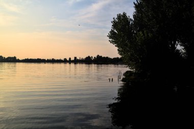 Gün batımında gölde ağaçların siluetiyle çerçevelenmiş.