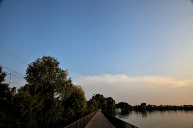 Gün batımında ağaçlarla çevrili bir göldeki geçit.