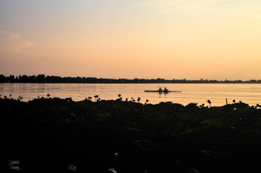 Gün batımında gölde ağaçların siluetiyle çerçevelenmiş.