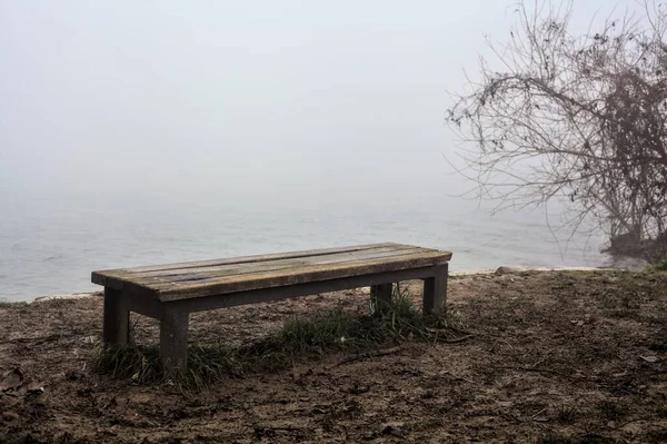 在意大利乡间的一个多雾的日子里 坐在一条没有树木的河边的长椅上 — 图库照片