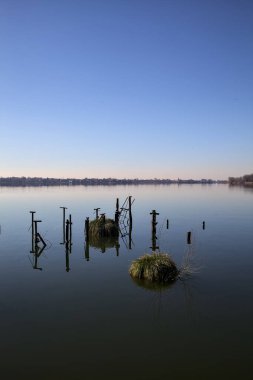 Aydınlık bir günde yansımaları olan bir gölde demirleme direkleri.