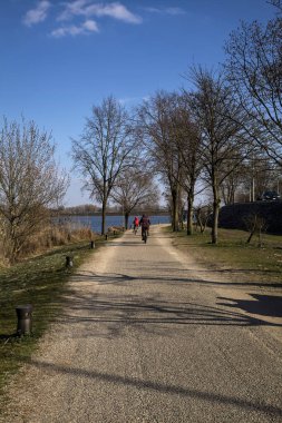 Gölün kıyısındaki bir parkta güneşli bir günde gezinen insanlarla dolu bir yol.