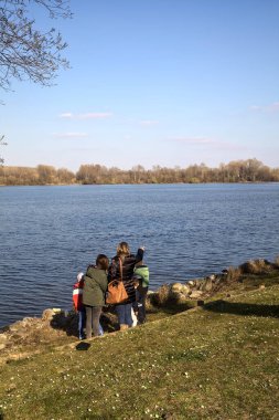 Güneşli bir günde, gölün kıyısında bir kütükte oturan insanlar.