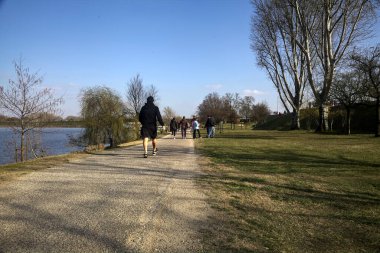 Gölün kıyısındaki bir parkta güneşli bir günde gezinen insanlarla dolu bir yol.