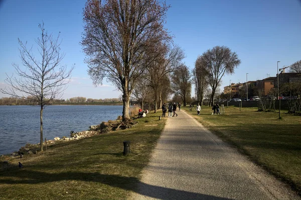Gölün kıyısındaki bir parkta güneşli bir günde gezinen insanlarla dolu bir yol.