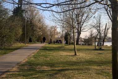 Gölün kıyısındaki bir parkta güneşli bir günde gezinen insanlarla dolu bir yol.