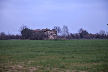 Terk edilmiş bir kır evinde, uzak bir tarlada, bulutlu bir günde, alacakaranlıkta.