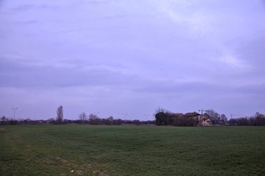 Terk edilmiş bir kır evinde, uzak bir tarlada, bulutlu bir günde, alacakaranlıkta.