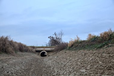 Bulutlu bir günde alacakaranlıkta İtalya kırsalındaki tarlalar arasındaki kuru su akıntısı