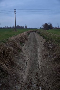 Bulutlu bir günde alacakaranlıkta İtalya kırsalındaki tarlalar arasındaki kuru su akıntısı