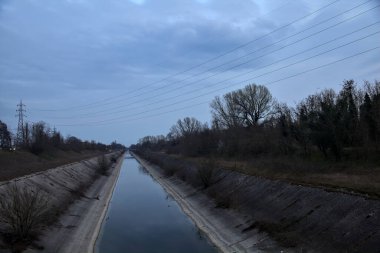Alacakaranlıkta bulutlu bir günde, gökyüzünün suya döküldüğü bir hava kanalı.