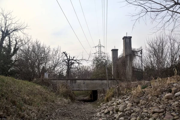 Karanlık çöktüğünde, bulutlu bir günde, bir kapısı ve çıplak ağaçları olan bir köy yolu.