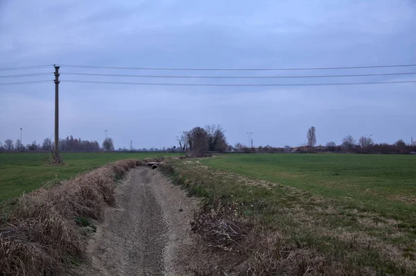 Bulutlu bir günde alacakaranlıkta İtalya kırsalındaki tarlalar arasındaki kuru su akıntısı