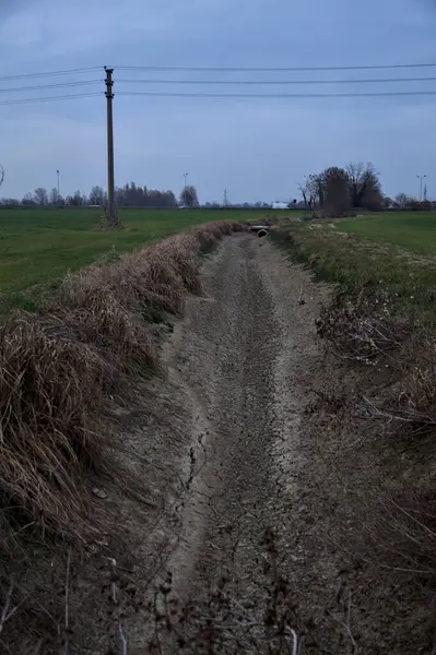 Bulutlu bir günde alacakaranlıkta İtalya kırsalındaki tarlalar arasındaki kuru su akıntısı