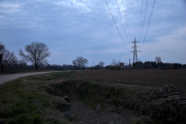 Bulutlu bir günde, alacakaranlıkta tarlaların yanındaki köy yolu.