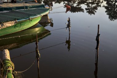 Yansımaları suya dökülen demirli tekne ve direkler.