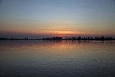 Bir gölün üzerinde gün batımı ve suya düşen gökyüzü.