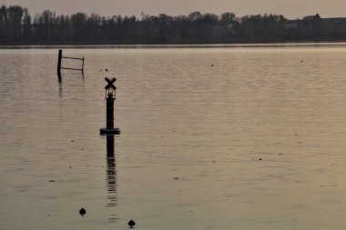 Gün batımında bir gölde şamandıra ve uzakta bir orman.