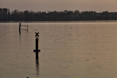 Gün batımında bir gölde şamandıra ve uzakta bir orman.