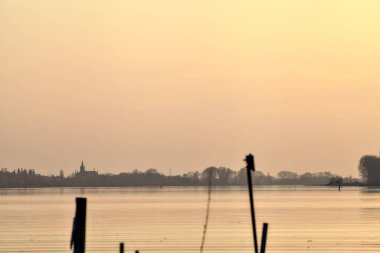 Gün batımında bir gölün kıyısında demirleme direkleri