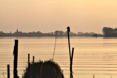Gün batımında bir gölün kıyısında demirleme direkleri