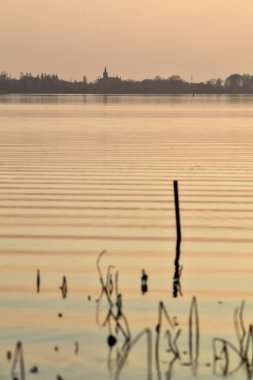Gün batımında bir gölün kıyısında demirleme direkleri
