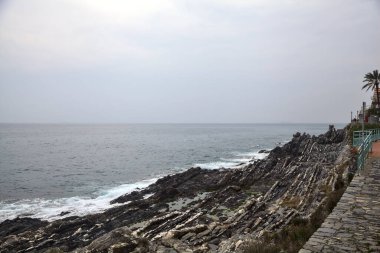 Bulutlu ve yağmurlu bir günde, deniz kıyısında binaları olan bir uçurumun kenarındaki patika.