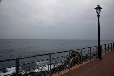 Bulutlu bir günde deniz kenarında sokak lambası olan panoramik patika