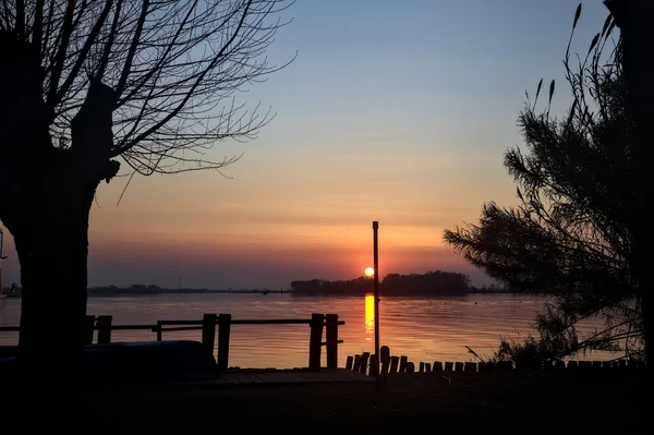 Sazlıklar tarafından çerçevelenmiş bir gölün üzerinde batan güneş.