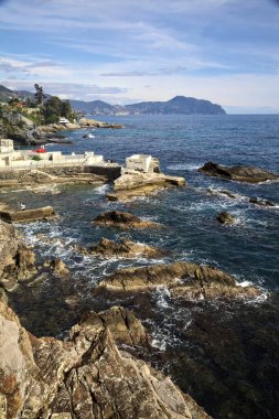 Güneşli bir günde deniz kenarında tarihi evler ve ağaçlarla dolu bir uçurum ve uzaktaki denize kadar uzanan bir kara şeridi.