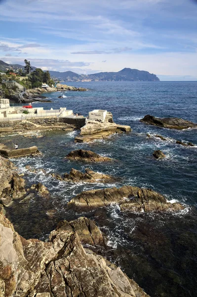 Güneşli bir günde deniz kenarında tarihi evler ve ağaçlarla dolu bir uçurum ve uzaktaki denize kadar uzanan bir kara şeridi.